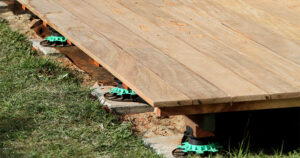Bord d'une terrasse en lames de bois surélevée sur plots réglables, posée sur gravier et pelouse