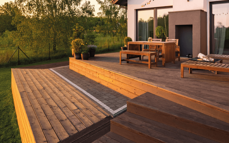 Terrasse en bois composite sur deux niveaux posée sur plots réglables, avec marche, table et bancs devant une maison moderne