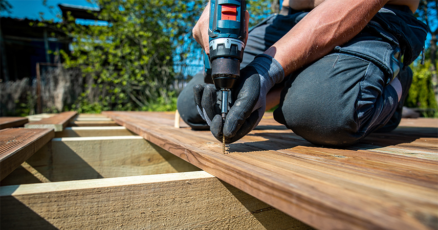 Bricoleur fixant une lame de terrasse en bois à la visseuse sur une structure posée au sol