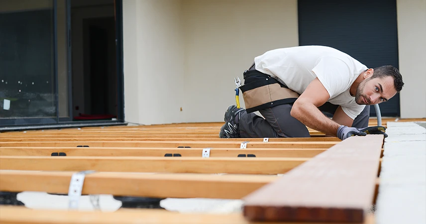 jeune homme qui monte une terrasse en bois sur plots